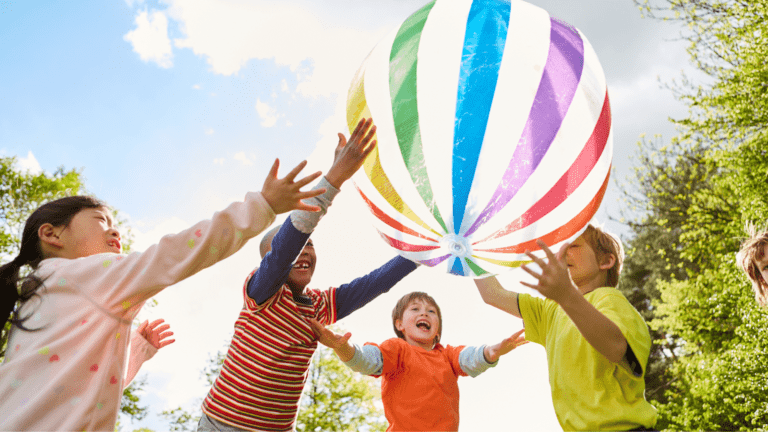 Excited children practicing non-verbal communication with a large colorful ball outdoors.